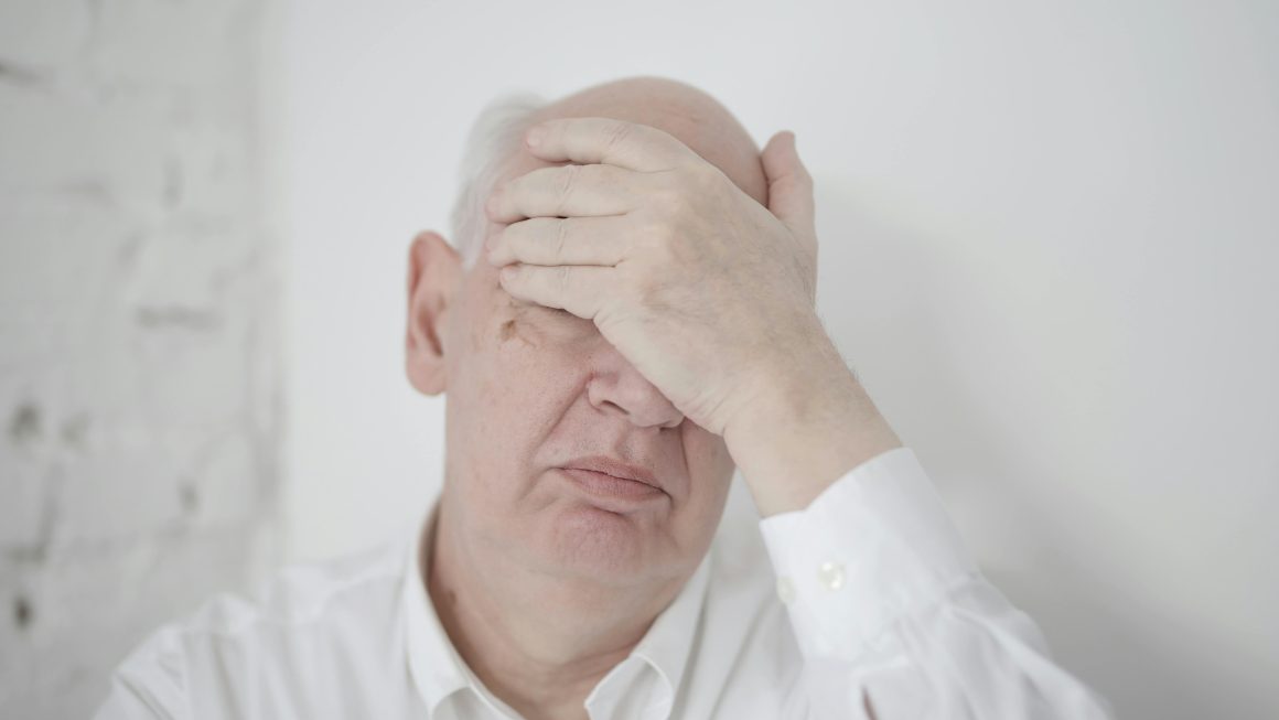 older man in pain, touching his forehead