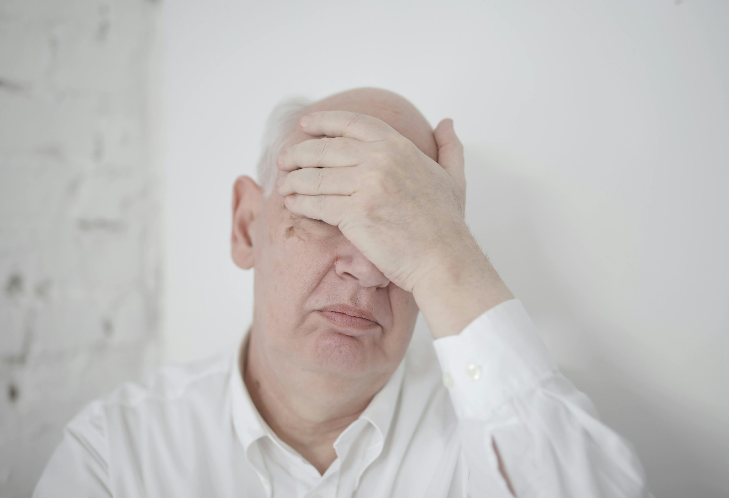 older man in pain, touching his forehead